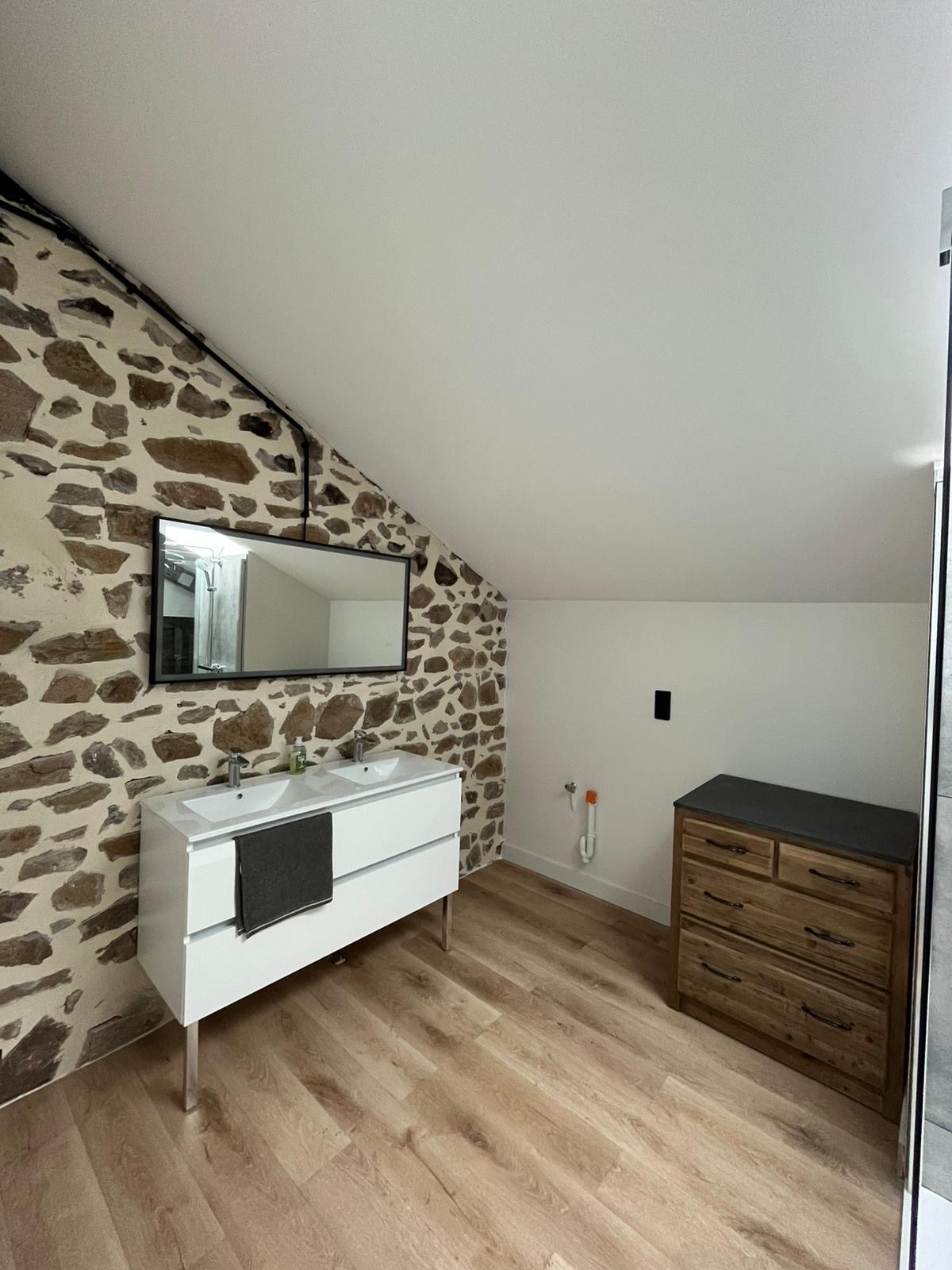 Meuble double vasque contre un mur en pierre, dans une salle de bain sous combles